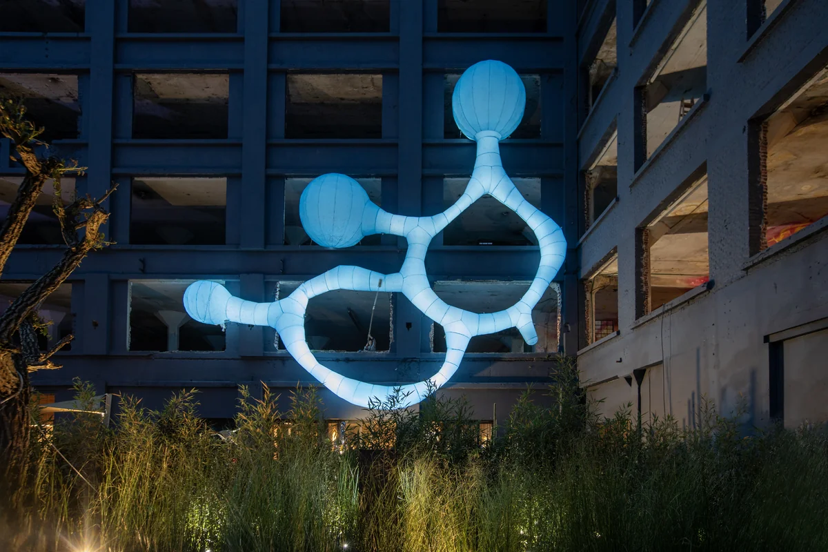 Estructura de hormigón con vanos vacíos, atravesada por un inflable celeste de tubos y esferas.