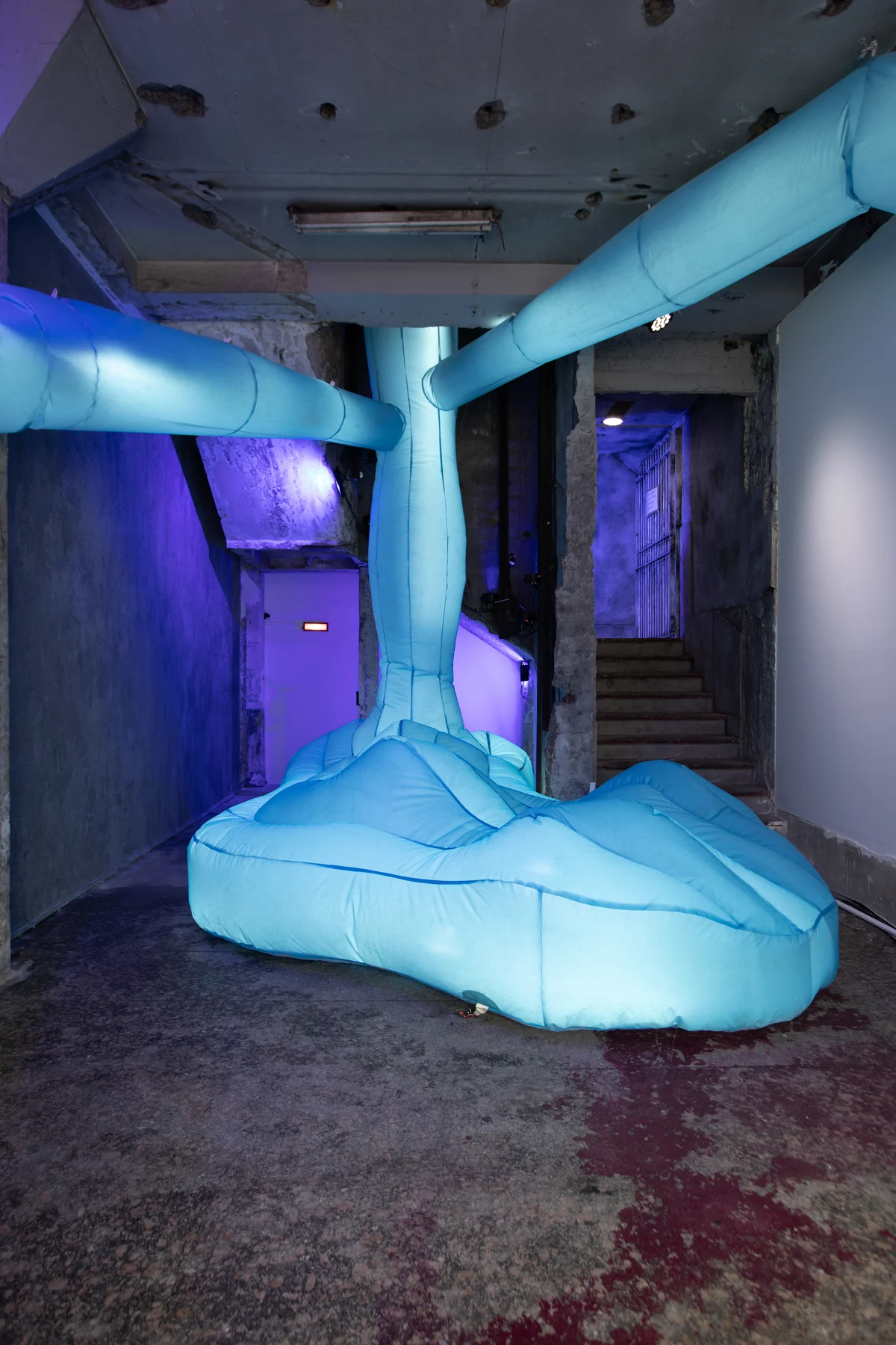 Pasillo con luz violeta: un tubo celeste baja del techo y se derrama en el piso.